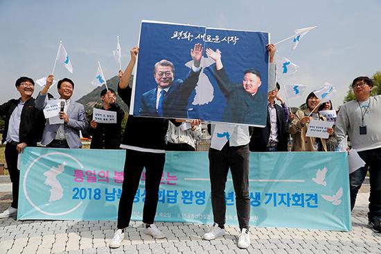 当地时间2018-06-23,韩国首尔,民众手持韩国总统文在寅与朝鲜最高领导人金正恩的海报参加游行,呼吁半岛和平。视觉中国 图