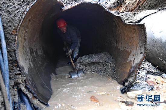 7月15日，在长春市南关区永长路，工人赵洪启在旧供热管内清理淤泥和积水。
