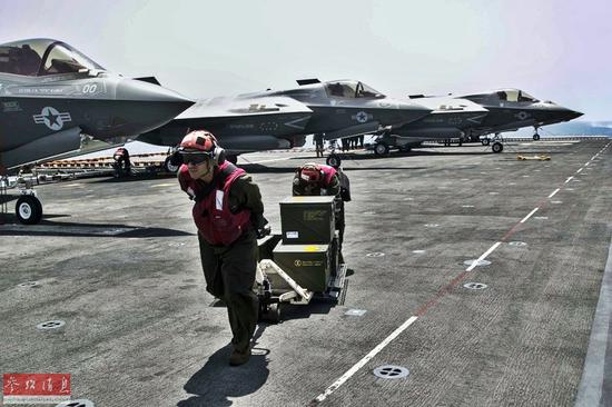 美海軍軍械官在飛行甲板上搬運彈藥，背景可見3架F-35B戰機。