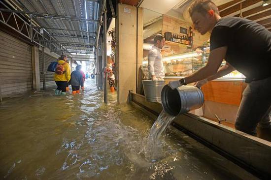 水位高涨下商店都被浸水，店主用桶排水（图片来源：ANSA）