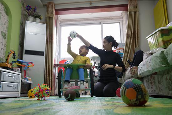 △ 2018年10月15日，北京市通州区，松子坐在自己的“小飞车”上玩球。”小飞车“是拜托病友姥爷依照美国患儿妈妈提供的图纸手工制作的，但它只有运动功能，没有辅助措施。