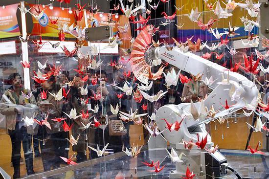 进博会智能及高端装备展区，一个拿着扇子在彩色纸鹤群中跳舞的工业机器人吸引着观众的目光。赖鑫琳 摄