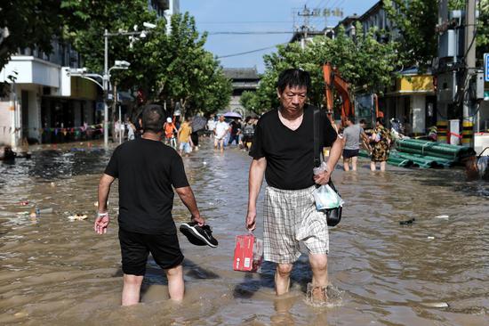 8月11日下午，临海部分路段仍有积水，一位市民在街上购买补给品后，趟水回家。新京报记者 王嘉宁 摄