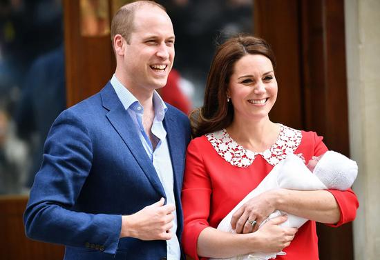 凯特王妃产后穿着一身红裙，脚踩裸色高跟鞋，怀抱小王子与丈夫威廉王子一起亮相。