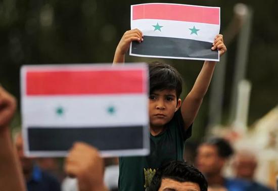 ▲4月15日，在伊拉克首都巴格达，人们手举叙利亚国旗参加集会。伊拉克民众15日在多地举行集会，抗议美国、英国、法国对叙利亚发动军事打击。（新华社/法新）