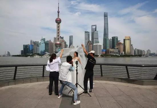 6月2日,上海外滩。新娘正以浦东新区陆家嘴的楼宇群为背景拍摄婚纱照。新京报记者 尹亚飞翻拍