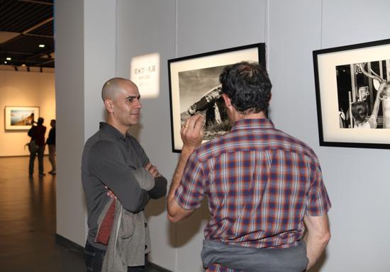 参展摄影师阿米尔·扎基（左一）与杰德 · 威尔加登在作品前交流。摄影：许瀚文