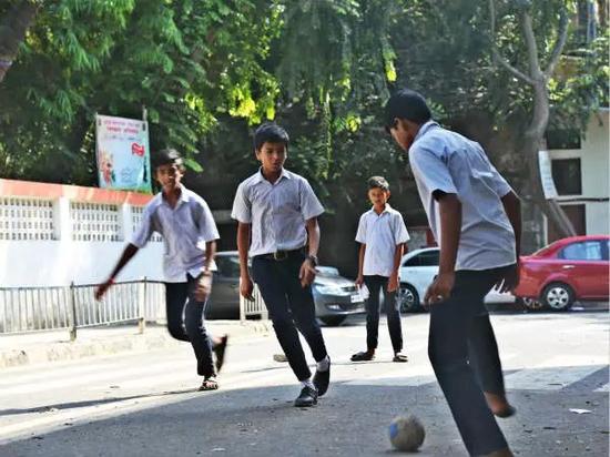公立学校的学生们在校门前穿着拖鞋和皮鞋踢足球。