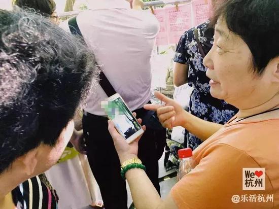 王阿姨在给相亲父母看手机里男孩的照片。