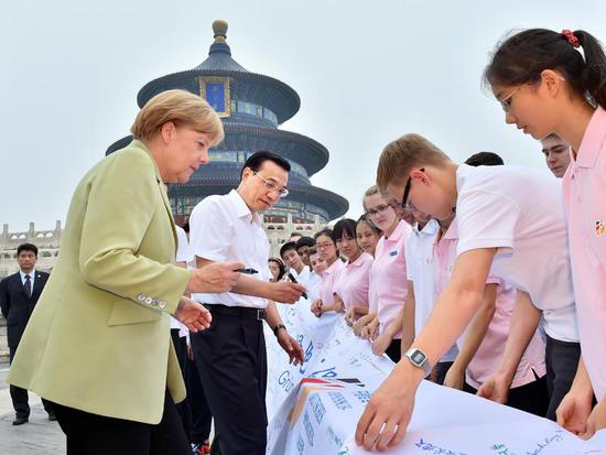 图为2014年7月7日，李克强总理同德国总理默克尔在北京天坛会见出席中德语言年闭幕式活动的两国青少年代表。这是李克强同默克尔在纪念横幅上签名。