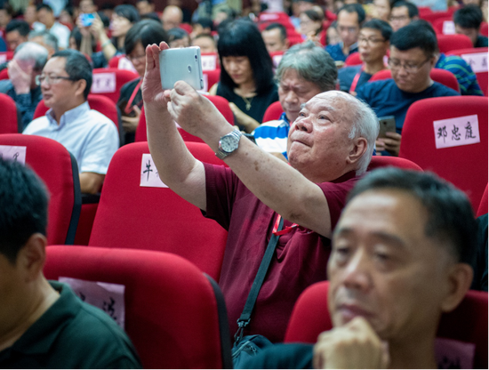 80多岁的老摄影家孙林杏正用手机拍摄开幕式