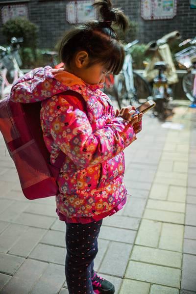 1月19日，在济南实验初中校门外，一位和姑姑来等表姐放学的小女孩，背着幼儿园的小书包，站在那里低头聚精会神地玩着姑姑的手机。视觉中国供图（资料图片）