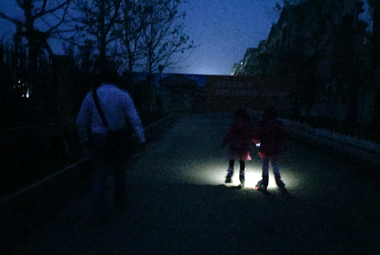 姐妹俩傍晚滑轮滑，蔡智奇怪用手机为孩子照着路面。