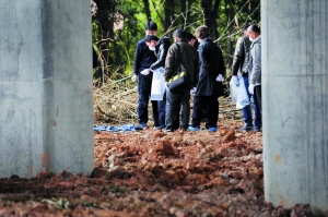 刑警在发现尸体的草丛里勘察现场，他们将提取的物证装入塑料袋。