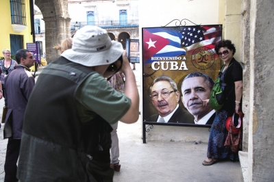 3月19日，一名游客在古巴一家餐馆门口的“奥巴马访古”宣传海报前拍照留念。图东方IC