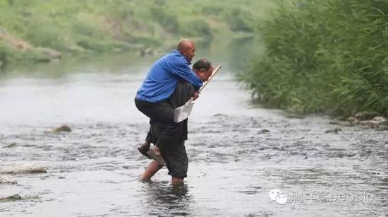 5月31日，贾文其背着贾海霞，趟水过河，到对岸的河滩植树。 新京报记者 尹亚飞 摄