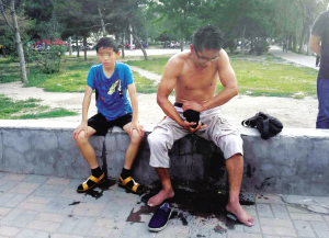 　　救人后，罗春江在桥边拧湿衣服，被救的男孩坐在他身边-晨报拍客 、杨先生供图