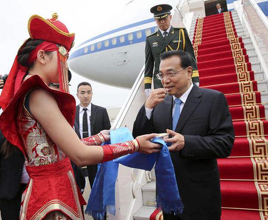 （7月13日，李克强总理抵达机场后，身着传统服饰的蒙古国女子向他献上哈达和奶干。新华社记者马占成摄）
