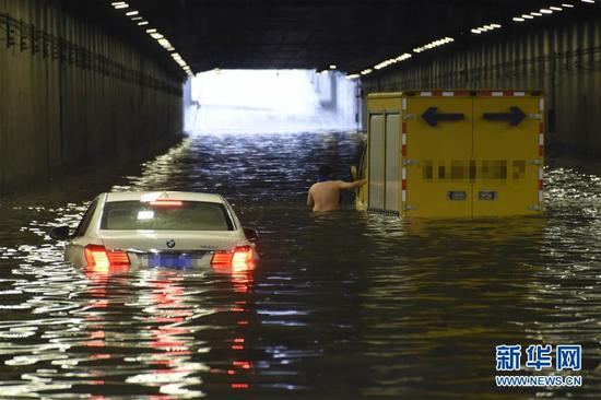 在北京西站北广场前主路隧道内，司机准备从被浸泡的车中撤离。