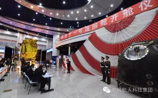 红白相间的巨型降落伞前，神舟十一号飞船返回舱“端坐”在宽敞的展厅里，层层相机的闪光灯围绕着它不停闪烁。