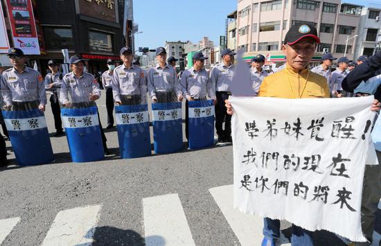 退休警员蔡荣仁（右）手拿“学弟妹觉醒！我们的现在，你们的将来”白布条，对着维持治安的警察诉求反对年金改革。（图片来源：台湾《联合报》）