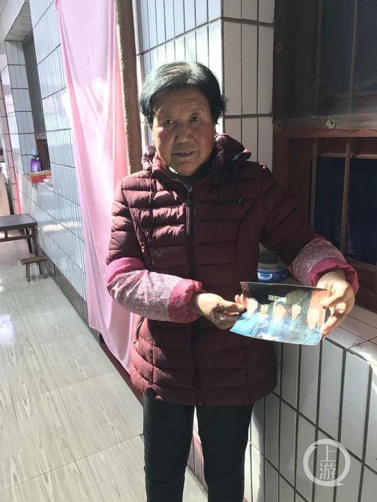 图为王琪弟媳拿着老家兄弟姐妹合影照片