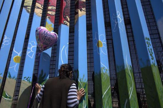 這是在墨西哥蒂華納拍攝的一名婦女隔着墨美邊境柵欄與女兒對話的資料照片。新華社發
