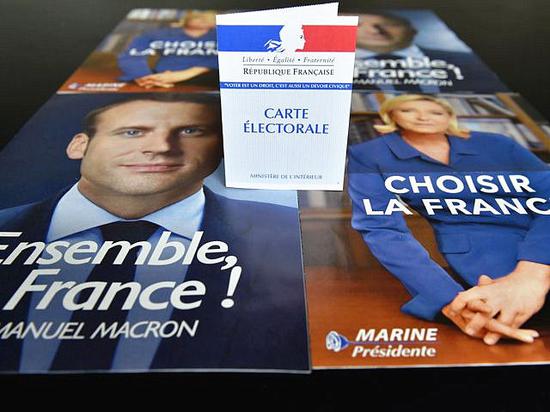 一张选民证摆放在法国总统候选人马克龙（左）和勒庞宣传画像上。（新华/法新）