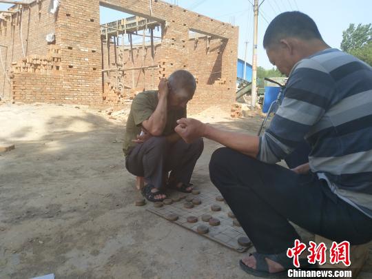 雄安新区小王营村一栋停建的平房前，两位村民正在下棋。王天译 摄