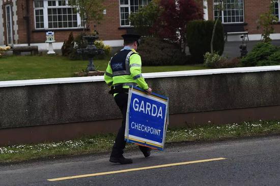 2017年5月12日，一名爱尔兰警察手持检查站标志牌，行走在爱尔兰和英国的边界附近。（新华社/路透） 