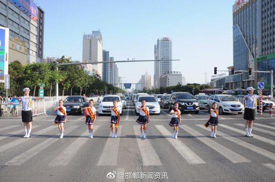 7月11日,河北邯郸市滏东大街与联纺路交叉口南北方向红灯亮起时,一阵“斑马线上亮红灯,请您等一等,红灯一会儿变绿灯……”音乐响起,小学生在女交警的带领下在斑马线前跳起了“等灯舞”。@邯郸新闻资讯 图