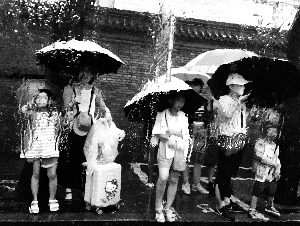 昨天，南长街，透过被雨水冲刷的窗玻璃，公交站上暑期旅游的家长和孩子幻化成了一幅水彩画。北京晨报记者 柴春霞/摄