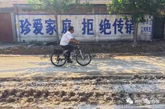 河北沧州新华区津德公路，一名男子骑着自行车经过一面“拒绝传销”宣传标语墙。新京报记者朱骏 摄