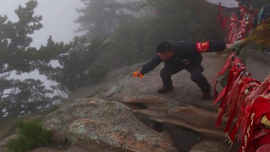 杜小利在华山西峰顶，翻越围栏捡游客丢弃的垃圾。