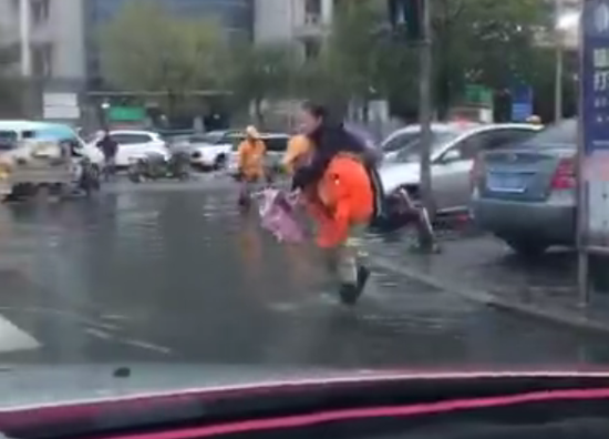 暖心！环卫工雨天涉水背路人过马路