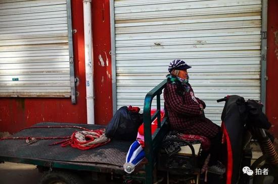 　　▲2017年11月22日，大兴区新建村，一位河南的老奶奶坐着自家的板车上，等着自己的工人在村中收旧家电回来。摄影/新京报记者彭子洋