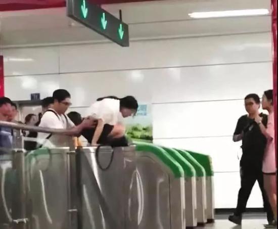 ▲一女子在男同伴的“扶助”下,爬过地铁检票闸机口。视频截图