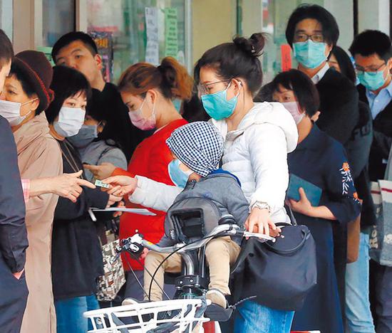  台湾实行实名制购买口罩，每人每周可买3只，图为妈妈带着小孩2日到药局排队买口罩。（图片来源：台湾“中时电子报”）