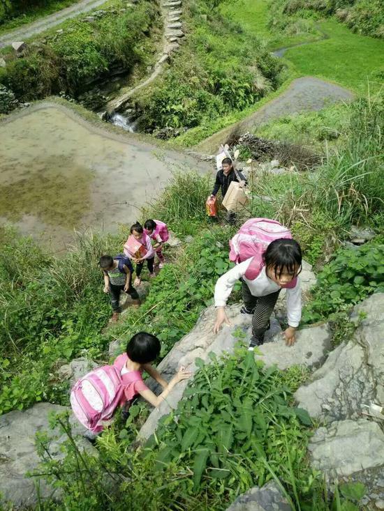 学生们每天上下学都要爬过山路，后面的吴艺伟则把免费营养餐一件件挑回学校。受访者供图