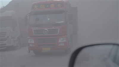 信发铝厂厂区外道路上,大货车来往不断,扬起粉尘。