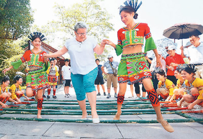 在海南三亚市南山景区，黎族阿妹和外国游客跳起竹竿舞。陈文武摄（人民图片）