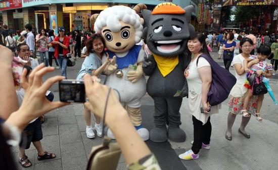 资料图：2010年6月19日，游客在台北西门町与大陆动画片主角“喜羊羊”、“灰太狼”的大型人偶一起合影。新华社