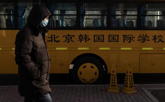 △ 3月4日，北京望京，戴口罩的行人经过北京韩国国际学校外的校车。