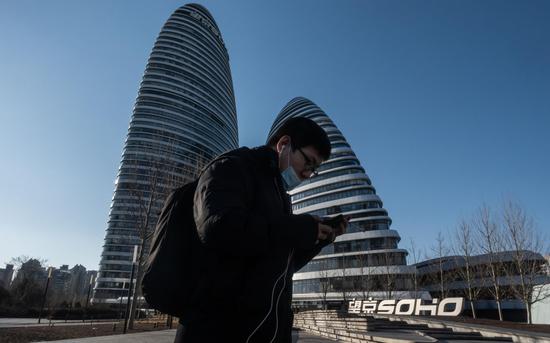 △ 3月3日，北京望京，市民戴口罩从标志性建筑银峰SOHO（原名望京SOHO）前经过。