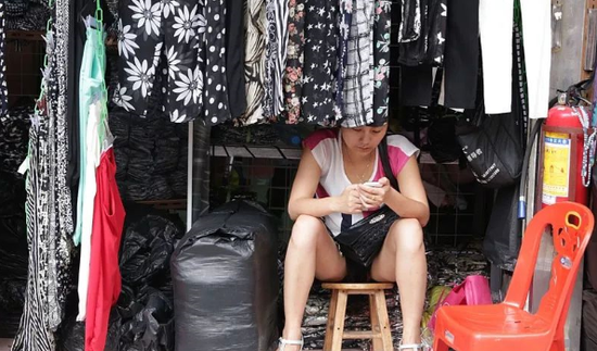 广州沙河顶服装市场，一名店主在空闲时间使用手机。