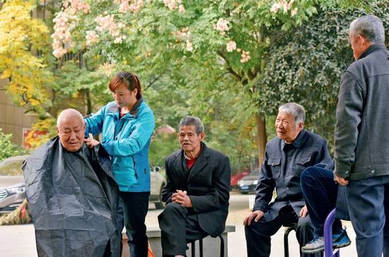 11月9日,在安徽省合肥市蜀山区井岗镇欣塘家园小区广场,47岁的李泽翠在为小区里的老年人免费理发。随着中国人口老龄化的加剧,养老金方面的需求日渐增长。图/视觉中国