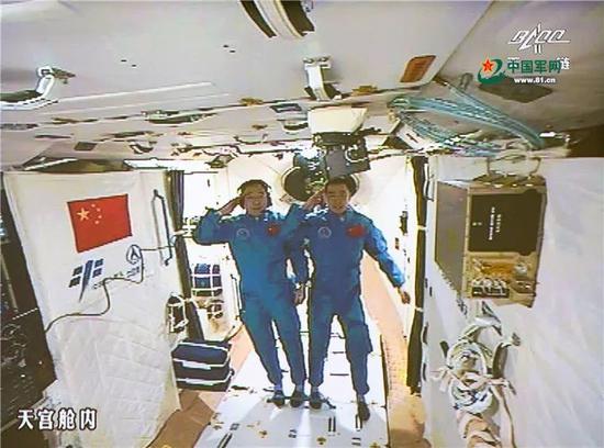 2016年10月19日,神舟十一号航天员景海鹏和陈冬顺利进入天宫二号实验舱。景海鹏(左)和陈冬在天宫二号实验舱向全国人民问好并敬礼(摄于北京航天飞行控制中心大屏幕)。