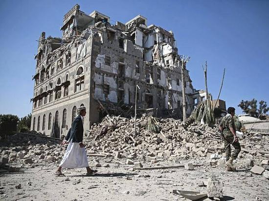 12月6日，也门首都萨那，胡塞武装人员从一栋在空袭中被炸毁的建筑旁走过。（新华/美联）