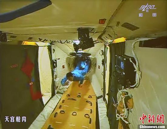 图为在张晓光的协助下,聂海胜顺利开启并进入天宫一号舱门(资料图)。中新社发 秦宪安 摄