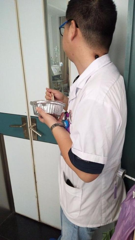 宋医生一边吃盒饭，一边盯着病房里的患者。  都市快报 图